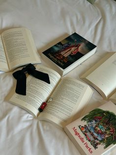 four open books on a bed with white sheets and black ribbon tied around the pages