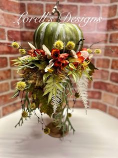 a vase filled with flowers and greenery on top of a white table next to a brick wall