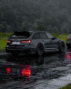 two audi cars parked in the rain on a wet road with trees in the background