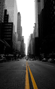 an empty city street with tall buildings and yellow lines painted on the road in front of it