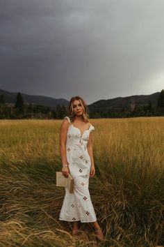 a woman in a white dress is standing in tall grass and looking at the camera