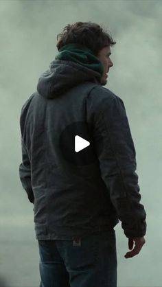 a man standing in front of a body of water wearing a black jacket and green scarf