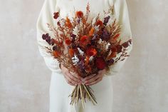 a woman holding a bouquet of dried flowers in her hands and looking at the camera