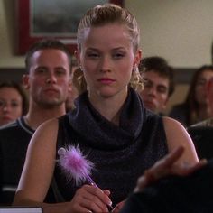 a woman sitting in front of a group of people with a pink feather on her finger