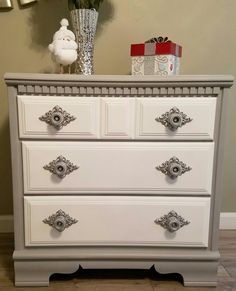 a white chest of drawers sitting on top of a floor next to a vase filled with flowers