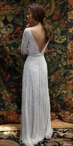 the back of a woman in a white dress standing against a wall with an ornate tapestry behind her