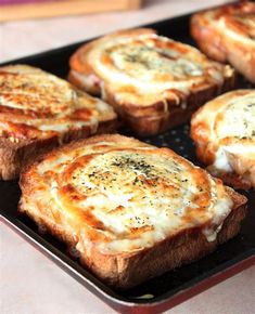 several pieces of bread topped with cheese and toppings on a black tray sitting on a table