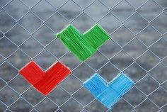 three different colored squares on a chain link fence