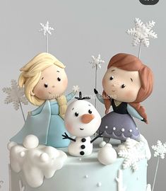 two figurines sitting on top of a frosted cake with snowflakes