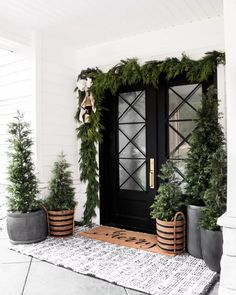 the front door is decorated for christmas with greenery and potted trees