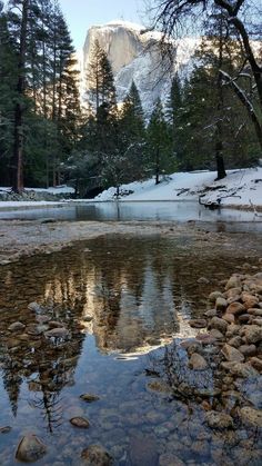 a small pond surrounded by rocks and trees with snow on the mountains in the background