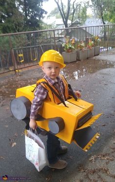 a little boy dressed up as a construction worker with a bag in his hand and wearing a yellow helmet