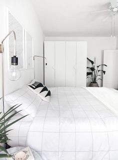 a bedroom with white bedding and plants in the corner