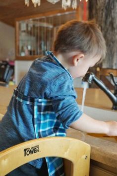 a young boy sitting at a kitchen counter in front of a sink and faucet