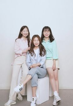 three young women sitting on top of a white box next to each other in front of a white wall