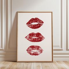 three red lipstick prints hanging on the wall in front of a wooden floor and white walls