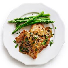 a white plate topped with meat covered in mushrooms and asparagus next to green beans