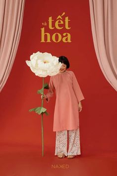 a woman standing in front of a red backdrop holding a white flower with the words tet hoa written on it