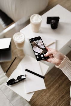 a woman holding up her phone to take a selfie with coffee and other items on the table