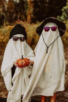 two people dressed in white and black with sunglasses on their heads, one holding a pumpkin