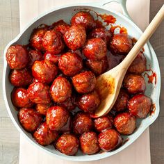 a wooden spoon sitting in a pot filled with meatballs and ketchup sauce