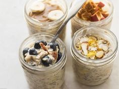 four jars filled with oatmeal and fruit on top of a white table