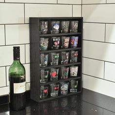 a wine bottle sitting next to a shelf filled with shot glasses on top of a black counter