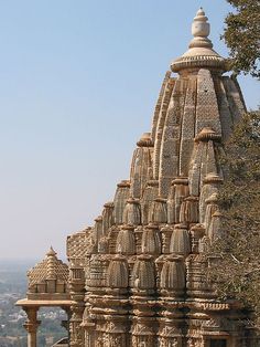 an intricately carved building with trees in the foreground and a city in the background