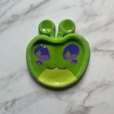 an apple shaped dish with purple and green designs on the front, sitting on a marble surface