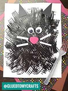 a paper plate with a cat made out of black crayons on it and a fork next to it