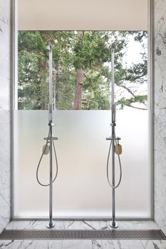 two shower heads in front of a large window with trees outside the windowsills