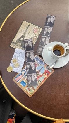 a cup of coffee sitting on top of a wooden table next to papers and coins