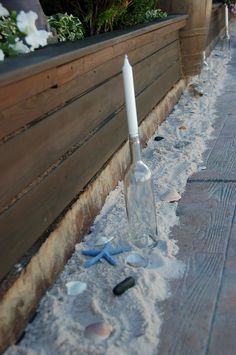 an empty glass bottle sitting in the sand next to a planter filled with flowers