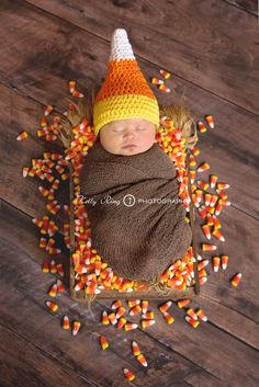 a newborn baby wearing a knitted hat and sleeping on corn cob surrounded by candy