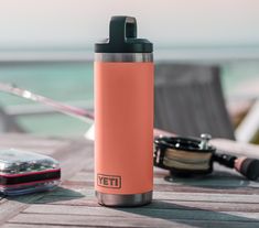 an orange yeti water bottle sitting on top of a wooden table next to a cell phone