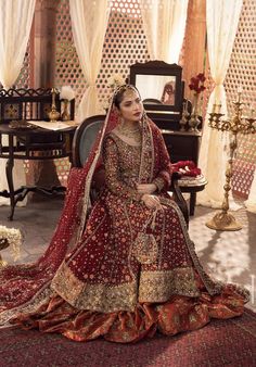 a woman sitting on top of a chair in a red and gold wedding dress with an elaborate