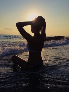 a woman is sitting in the water at sunset