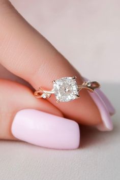 a woman's hand with a pink manicured nail and an oval shaped diamond ring