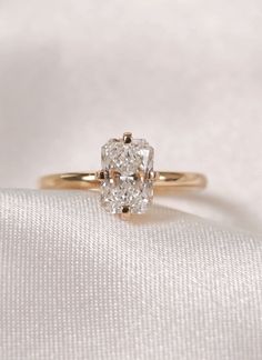 an oval cut diamond sits on top of a white cloth in front of a gold ring