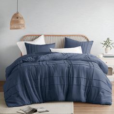 a bed with blue comforter and pillows on top of it, next to a lamp