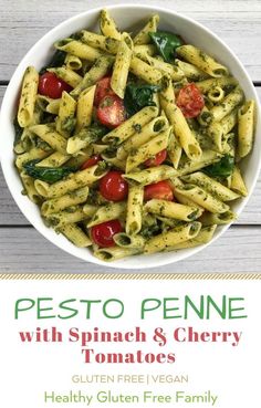 pesto penne with spinach and cherry tomatoes in a white bowl on a wooden table