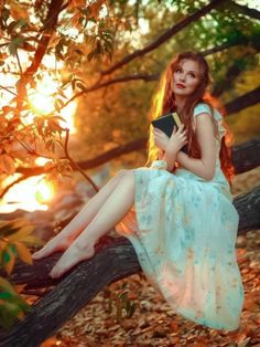 a woman is sitting on a tree branch with a book in her hand and the sun behind her