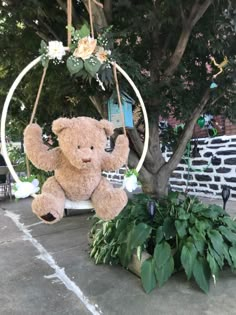 a teddy bear sitting on a swing in the middle of a yard next to some plants