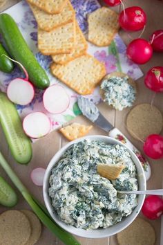 a bowl of spinach dip surrounded by crackers, radishes and cucumbers