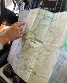 a person holding a map in their hand while sitting in a car with the steering wheel behind them