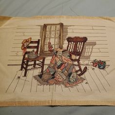 a cross - stitched picture of an old rocking chair and teddy bear on the floor