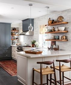 a kitchen with gray cabinets and white counter tops, two stools in front of the island