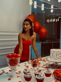 a woman standing in front of a table filled with cupcakes and red roses