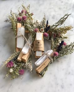 three wooden sticks with soaps tied to them sitting on a marble counter top next to dried flowers