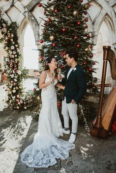 a newly married couple standing in front of a christmas tree and playing the harp together